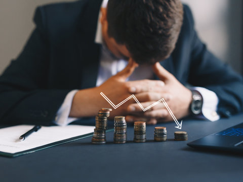 A stressed businessman in a suit sitting behind declining stacks of coins with a downward arrow, symbolizing financial loss and bankruptcy in San Jose.
