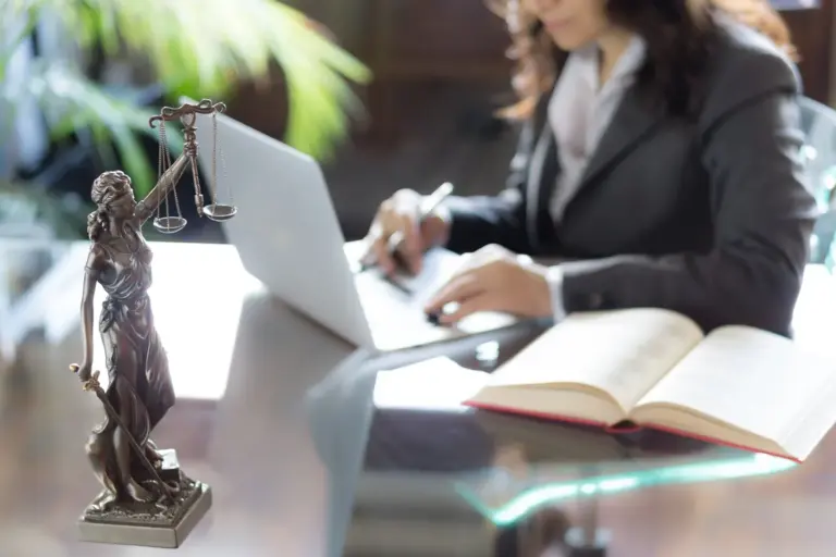 A professional woman preparing legal documents on a laptop beside a Lady Justice statue, symbolizing access to the legal system through trusted document assistance.
