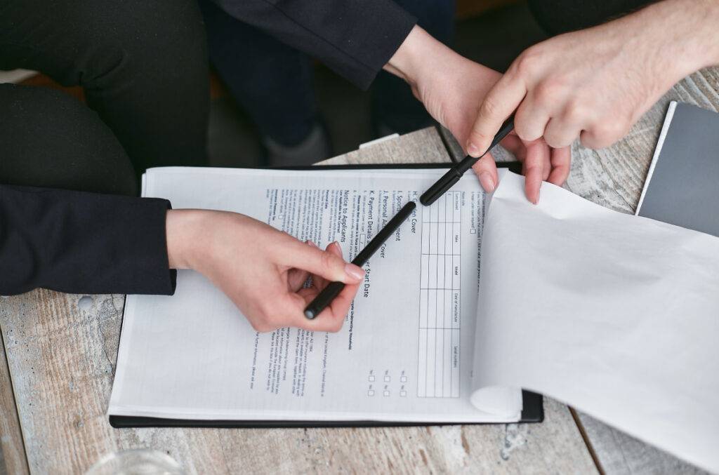Hands pointing to a legal document, reviewing details for accurate completion or translation—legal document preparation assistance in progress.