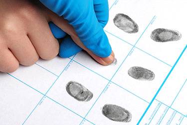 Ink fingerprint being rolled onto an FD-258 fingerprint card for background check or official identification.