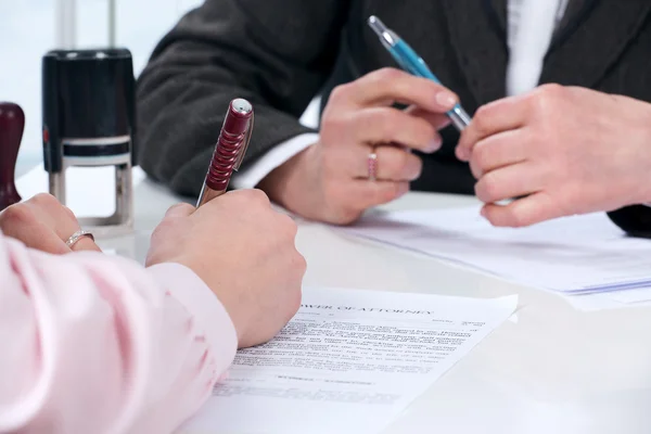 Two individuals signing and reviewing a Power of Attorney document during a legal consultation