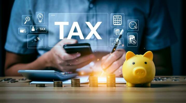 Person using calculator and phone for tax planning with coins and piggy bank, symbolizing business startup strategy.