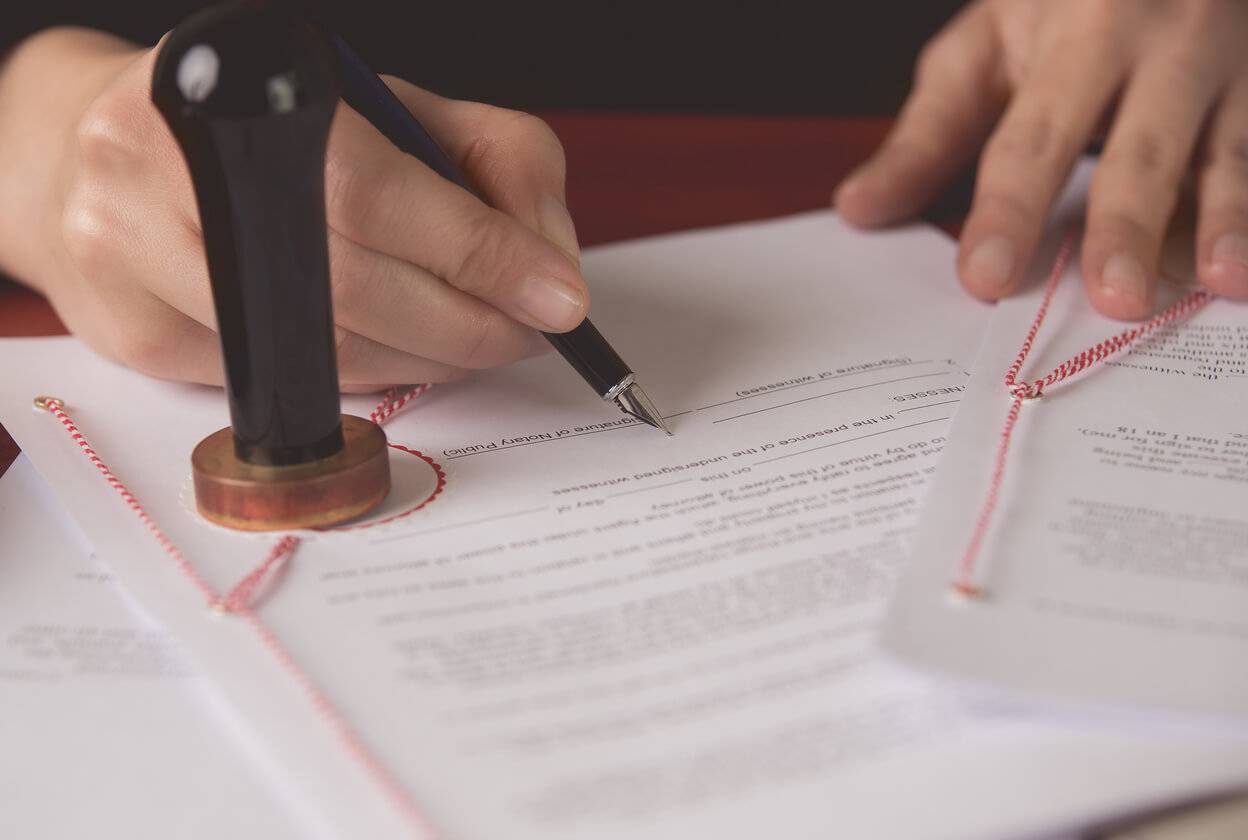 Person signing an official document with a seal and string binding, symbolizing apostille and notary certification