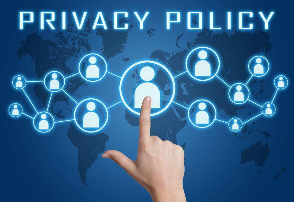 A hand pressing the digital privacy icon on a glowing blue world map with the word" Privacy Policy above it.
