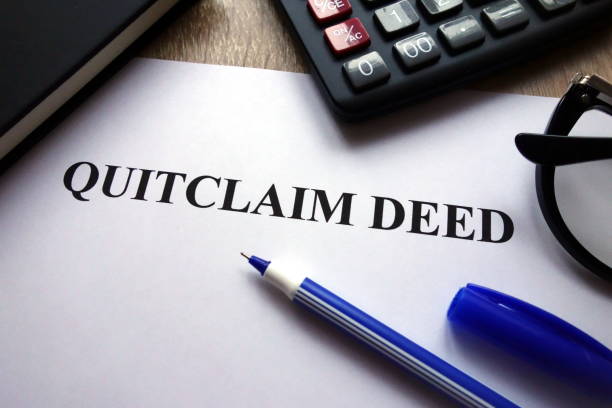 A quitclaim deed document on a desk with a pen, calculator, and eyeglasses, symbolizing property ownership transfer.