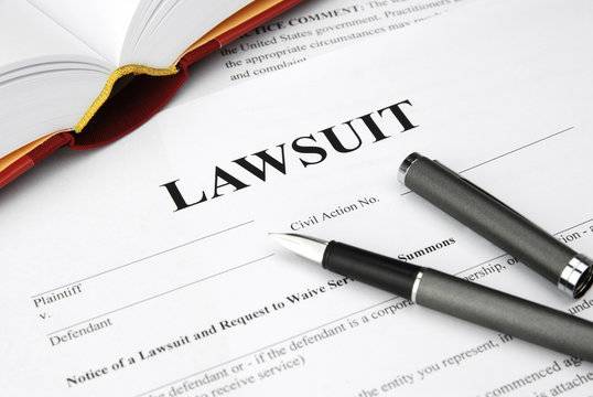 Close-up of a lawsuit document with pens and an open legal book on a desk.