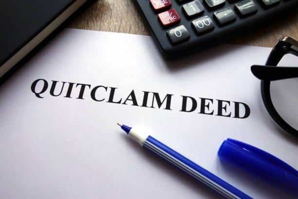 Quitclaim deed document with pen, calculator, and glasses — deed transfer services and legal document preparation.