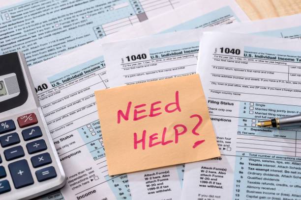 Tax forms with sticky note reading Need Help, calculator and pen on IRS 1040 paperwork.