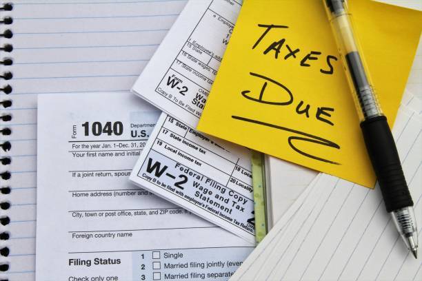 IRS 1040 tax form with W-2 statements, notebook, pen, and sticky note reading Taxes Due
