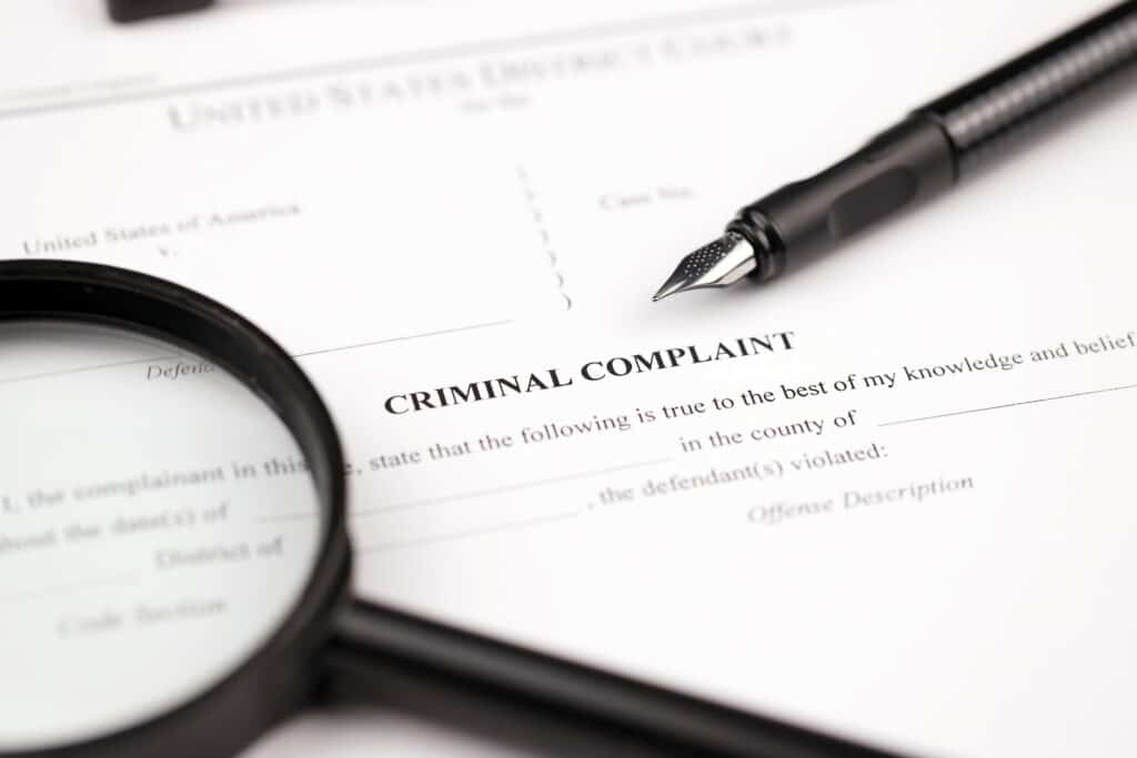 Criminal complaint court papers on A4 tablet lies on office table with pen and magnifying glass close up